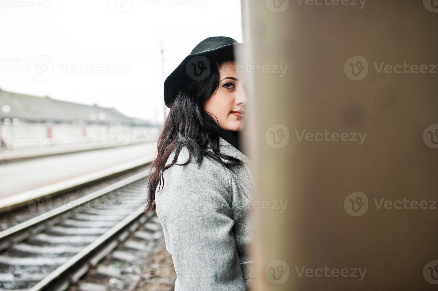 Brunette girl in gray coat with hat in railway station. photo