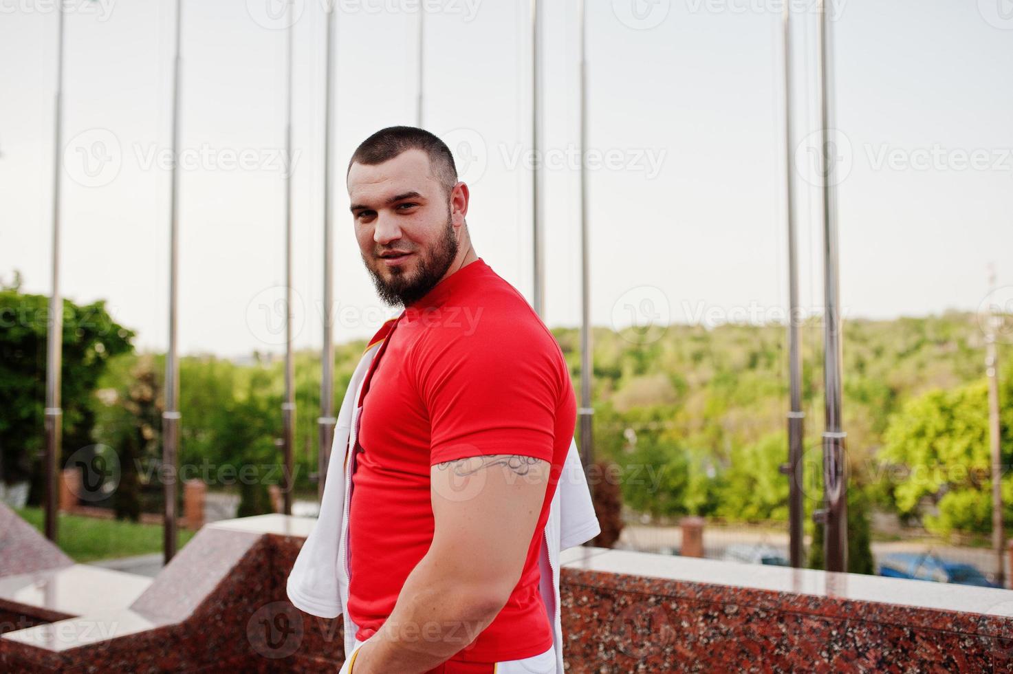 joven musculoso barbudo brutal vestido con traje deportivo blanco con camisa roja. foto