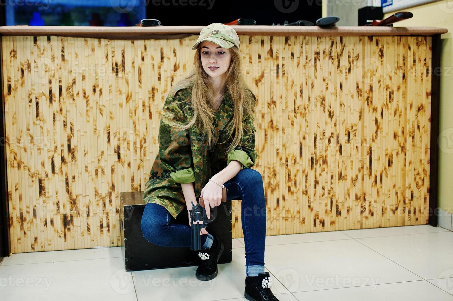 Military girl in camouflage uniform with revolver gun at hand against army background on shooting range. photo