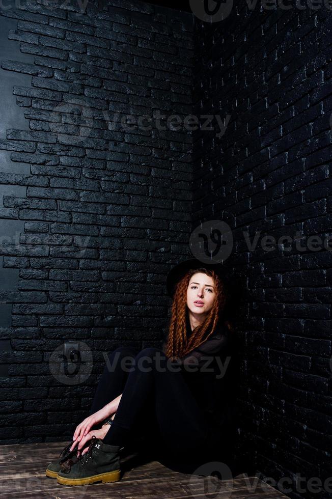 Studio shoot of girl in black with dreads and hat on brick background. photo