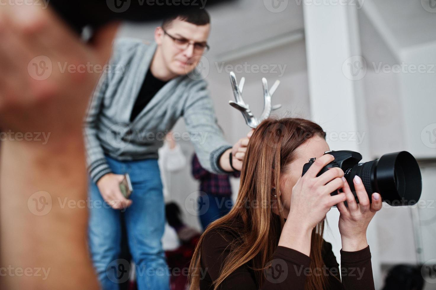 The team of two photographers shooting on studio. Professional photographer on work. One of them joking and holds horns over head. photo