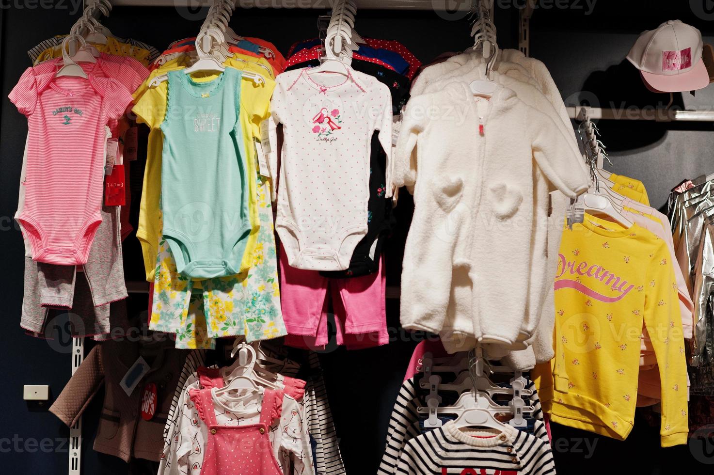 Children's bright clothes hang on the display in the baby clothing store. Girls section. photo