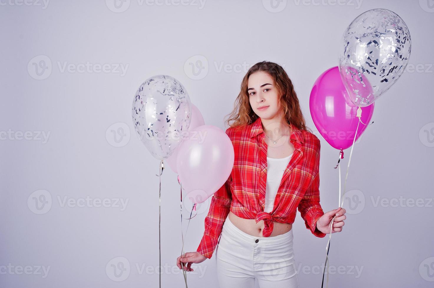 Young girl in red checked shirt and white pants with balloons against white background on studio. photo