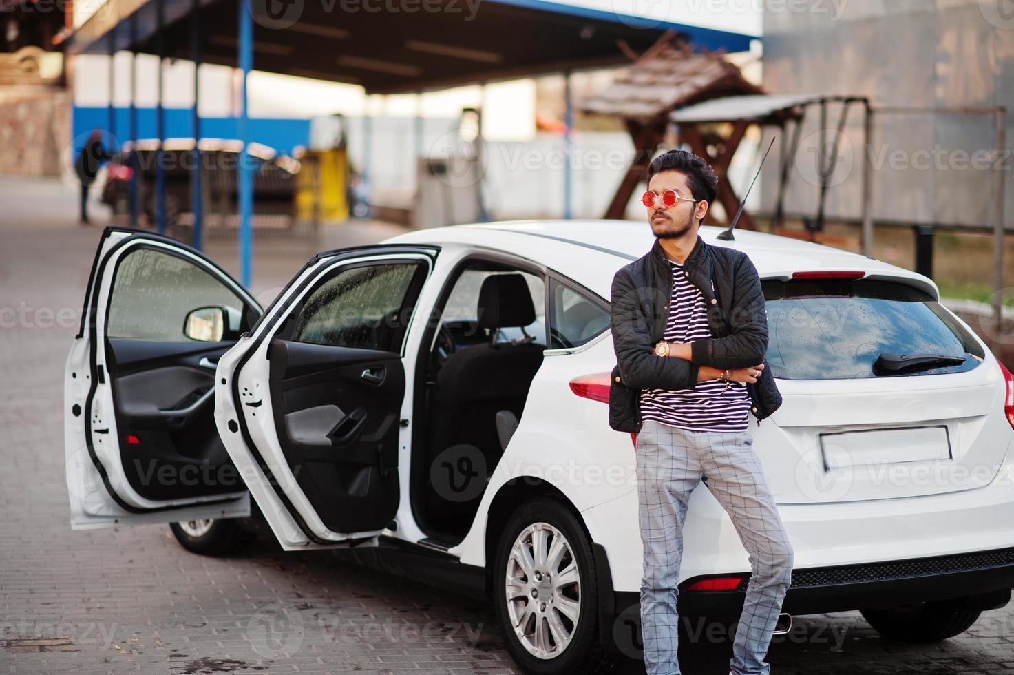 South asian man or indian male wear red eyeglasses stand near his white transportation on car wash. photo