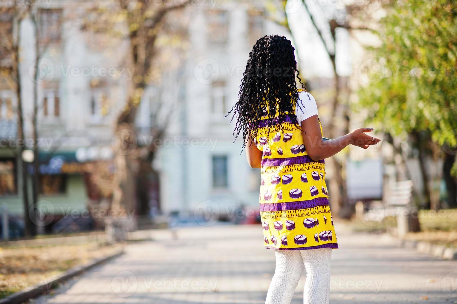 Stylish african american women in yellow jacket posed on street at sunny day with mobile phone at hand. photo