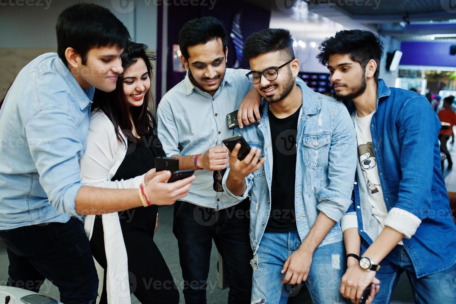 Group of stylish asian friends wear on jeans looking at mobile phones in club. photo