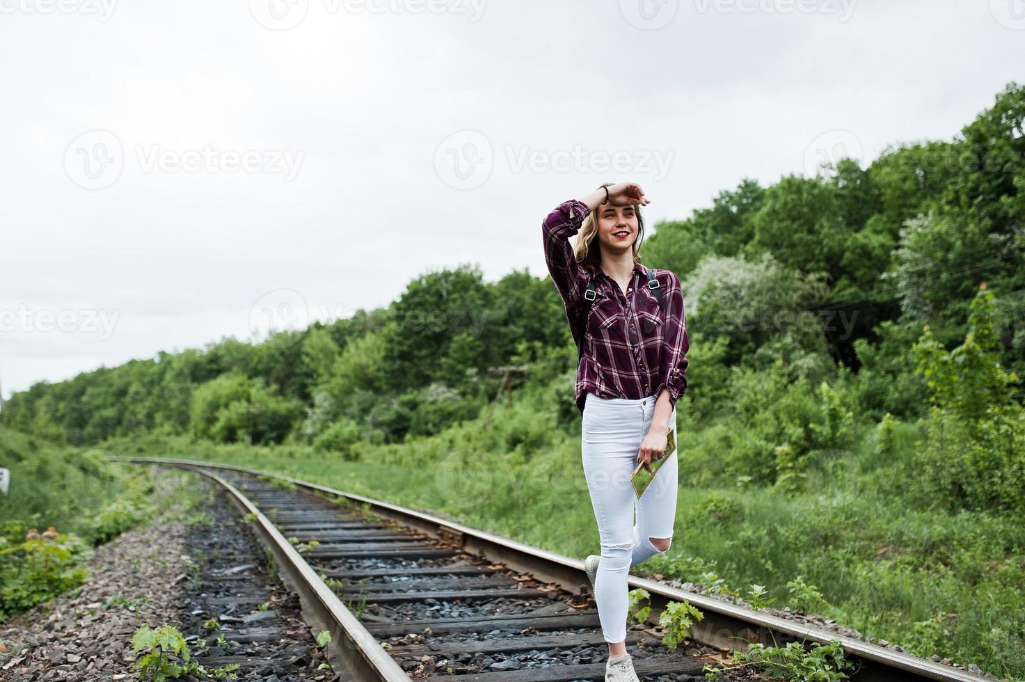 retrato de una linda chica rubia con camisa de tartán caminando por el ferrocarril con un mapa en las manos. foto