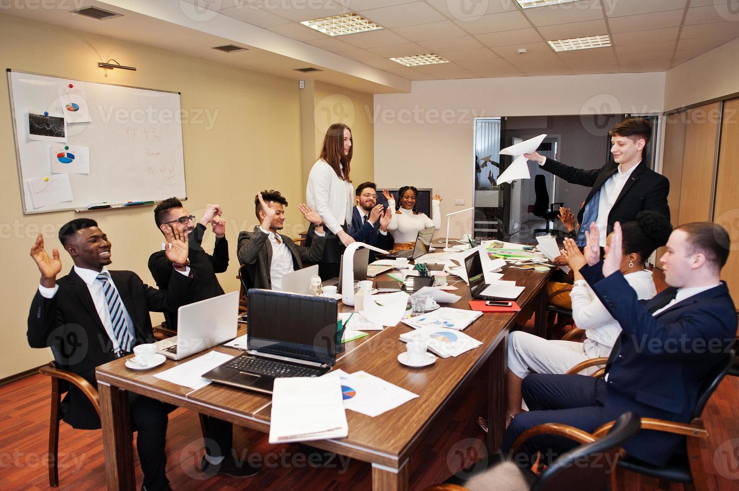 Multiracial business team meeting around boardroom table, two team leaders throw paper up. photo