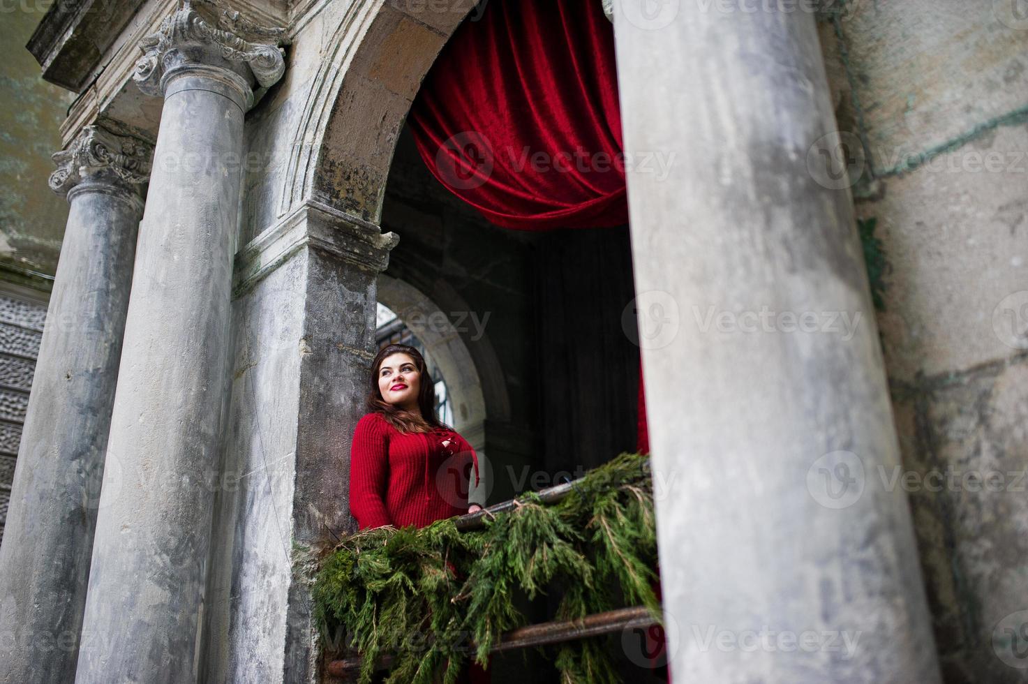 Brunette plus size model at red against arch with curtains. photo