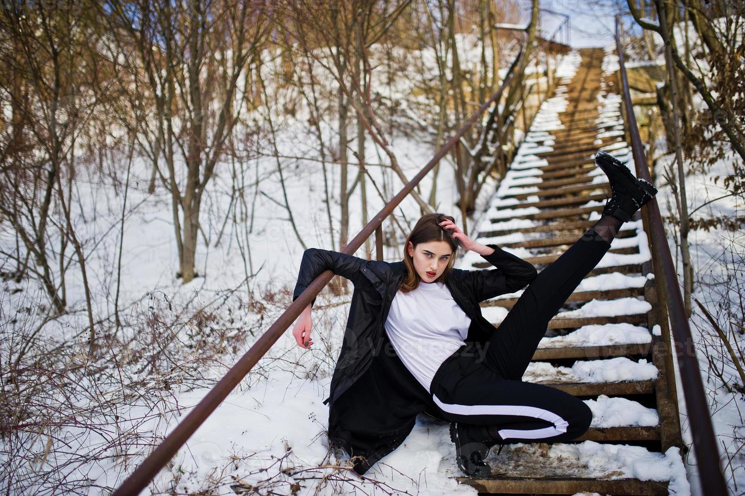 Fashionable long legs brunette model in long black cloak posed outdoor at winter day. photo