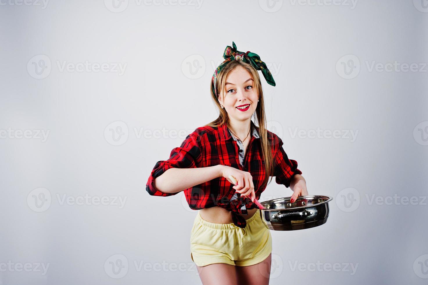 Young funny housewife in checkered shirt and yellow shorts pin up style with frying pan isolated on white background. photo