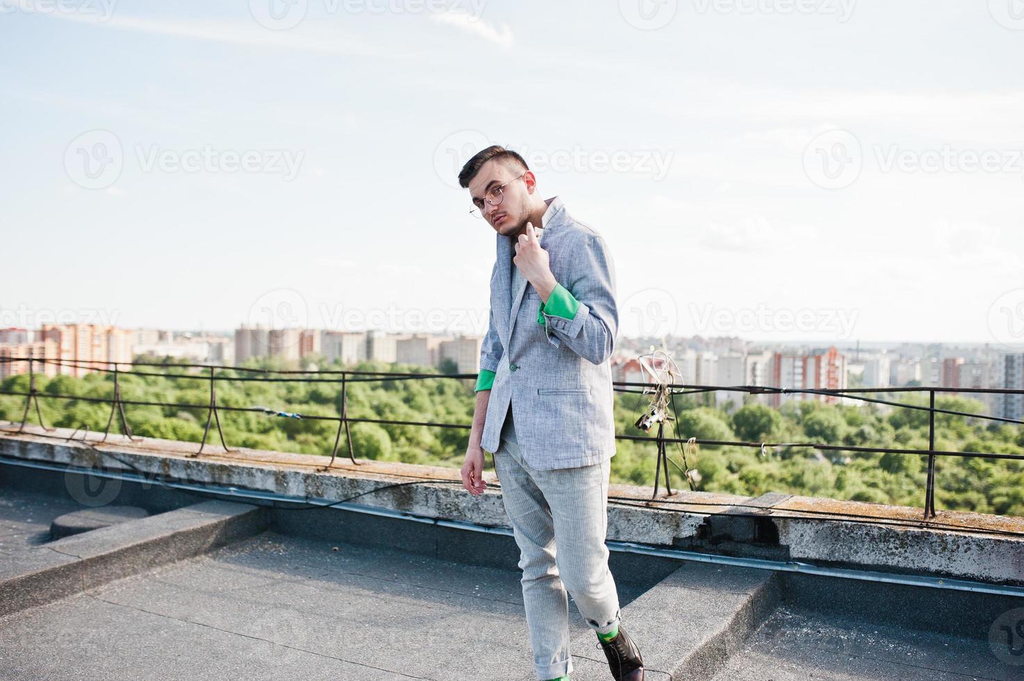 Dreamer stylish macho man in gray suit and glasses posed on the roof. photo