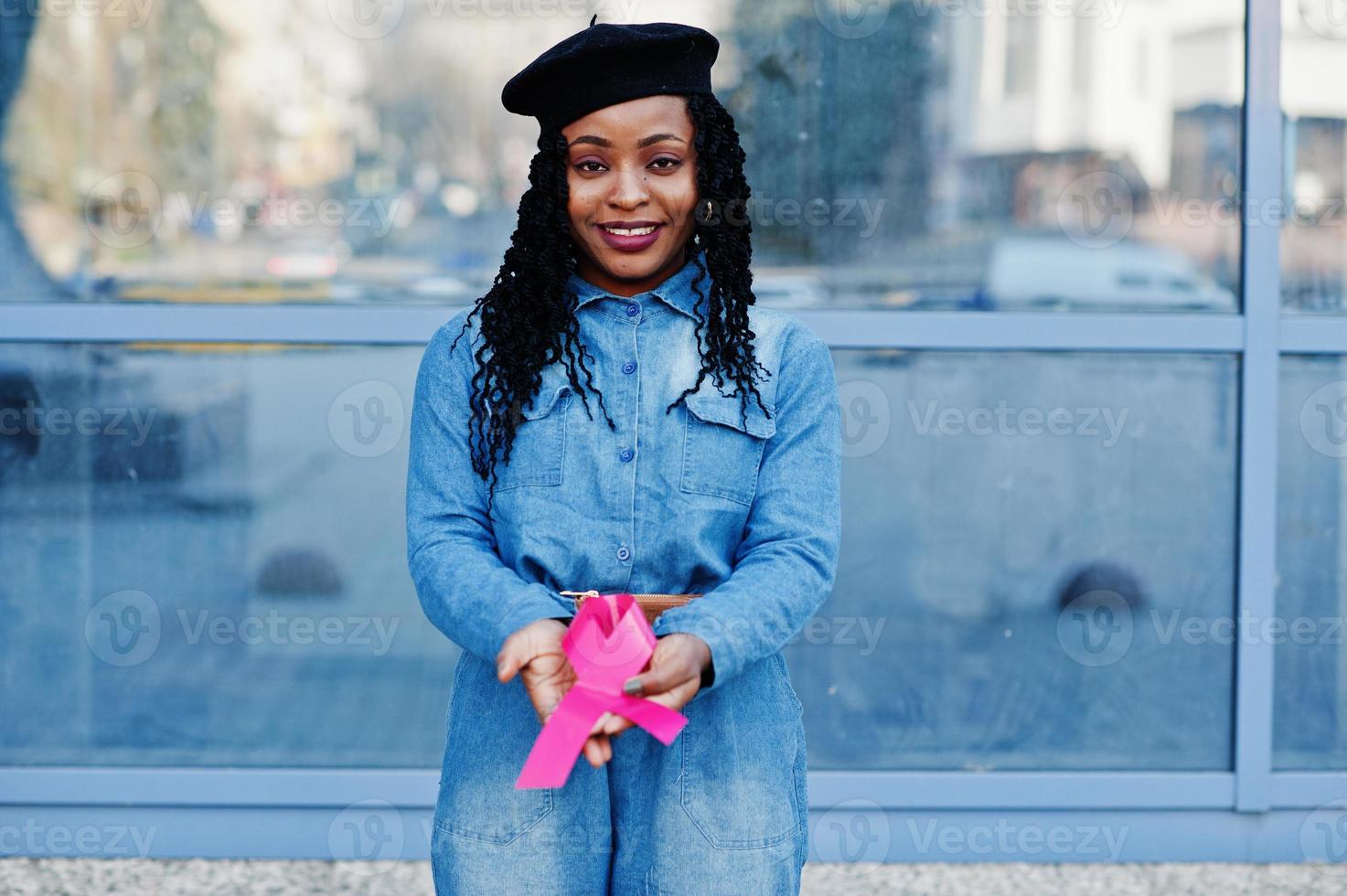 The power to fight. Stylish fashionable african american women in jeans wear and black beret against modern building with pink ribbon for breast cancer. photo