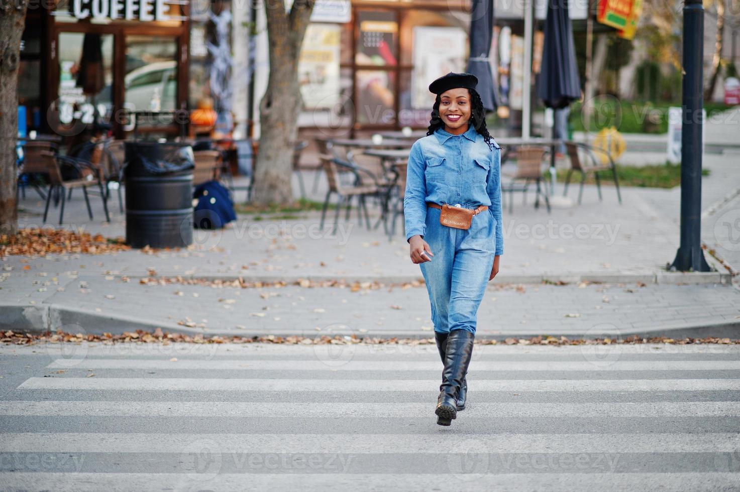 Stylish fashionable african american women in jeans wear and black beret walking on pedestrian traffic. photo