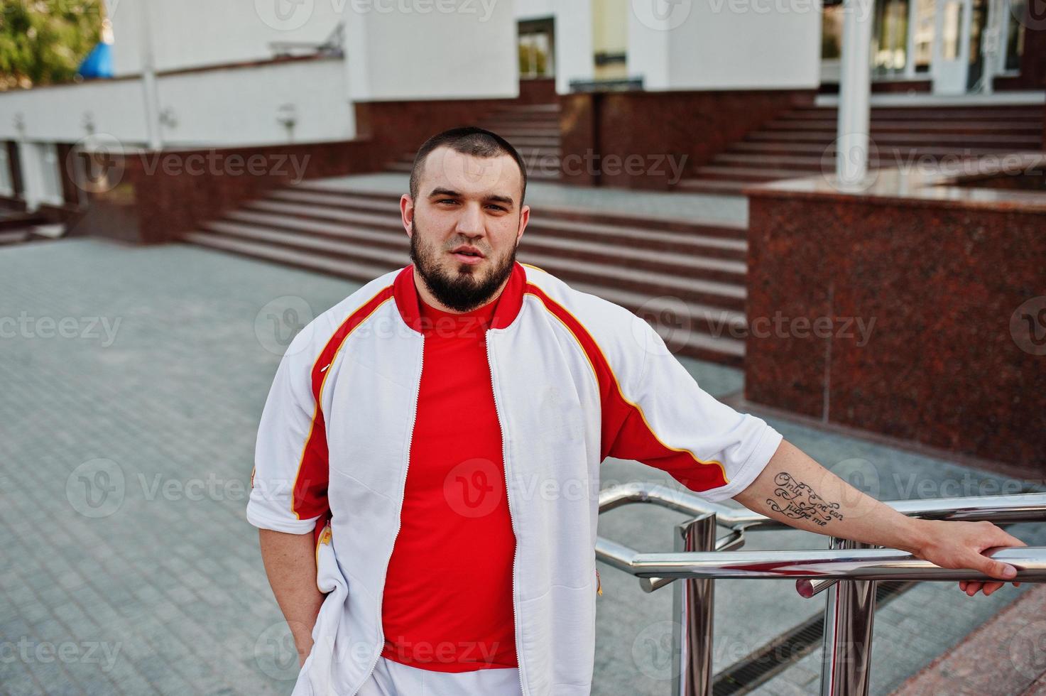 joven musculoso barbudo brutal vestido con traje deportivo blanco con camisa roja. foto