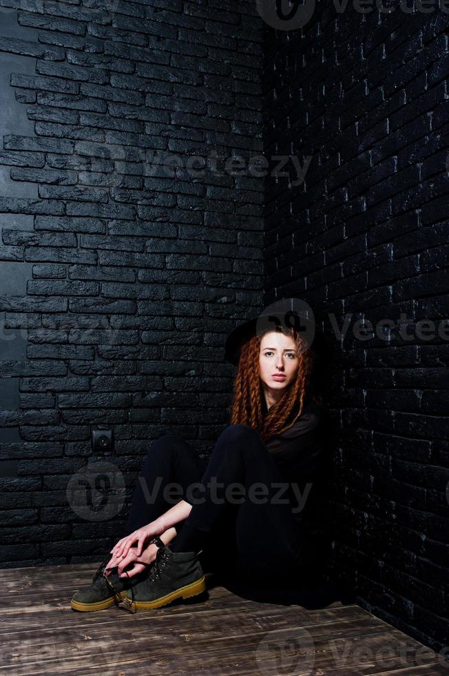 Studio shoot of girl in black with dreads and hat on brick background. photo