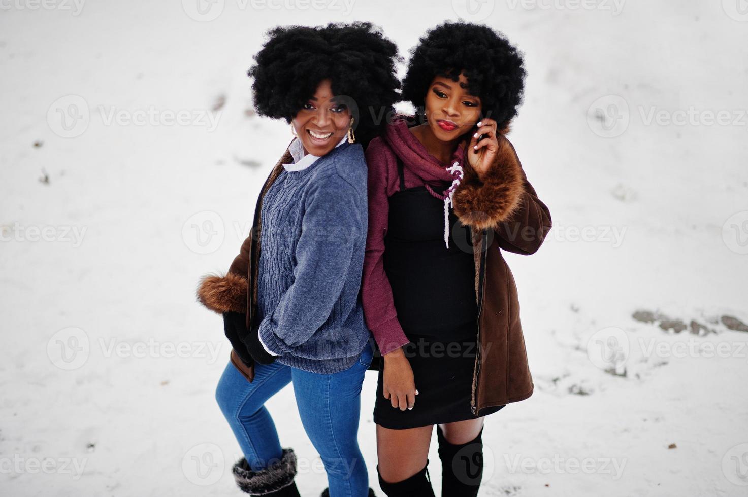 Two curly hair african american woman wear on sheepskin coat and gloves posed at winter day, speaking on phone. photo