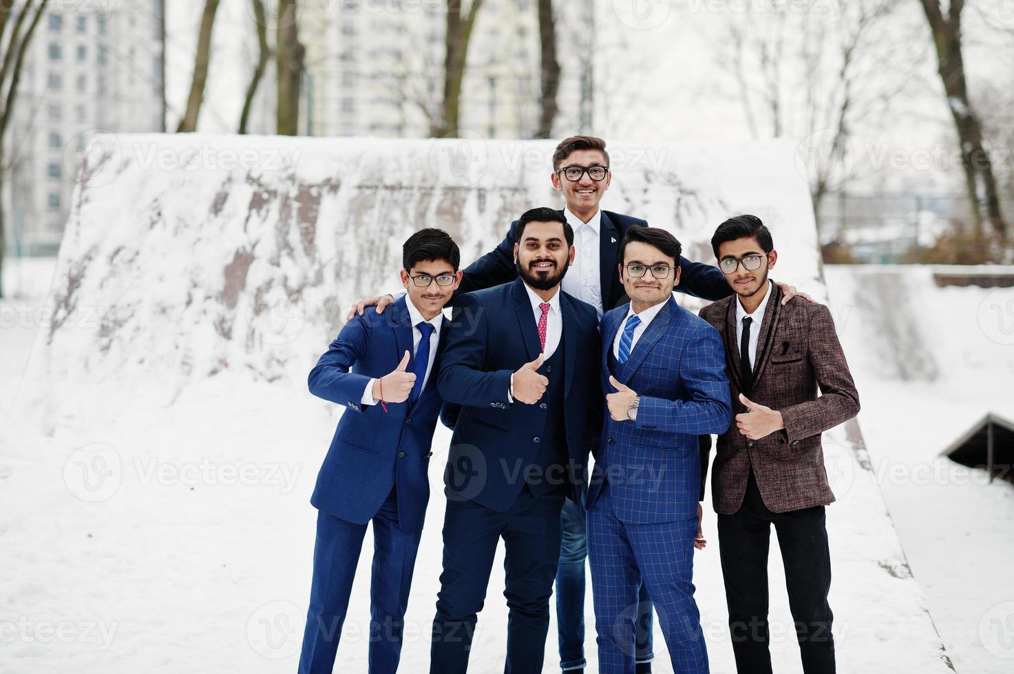 grupo de cinco hombres de negocios indios en trajes posados al aire libre en un día de invierno en europa, muestran el pulgar hacia arriba. foto