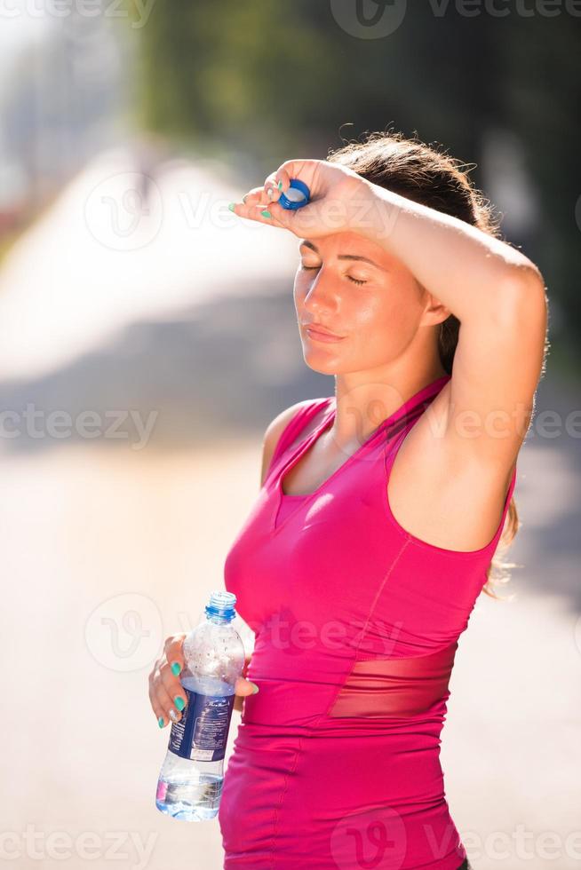 woman drinking water from a bottle after jogging photo