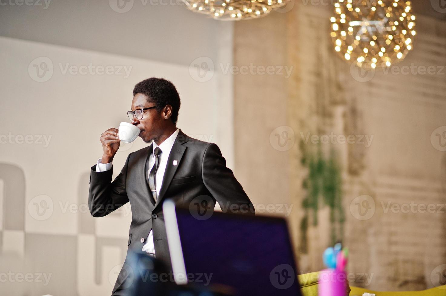 Business african american man wear on black suit and glasses at office, drinking morning coffee before work day. photo