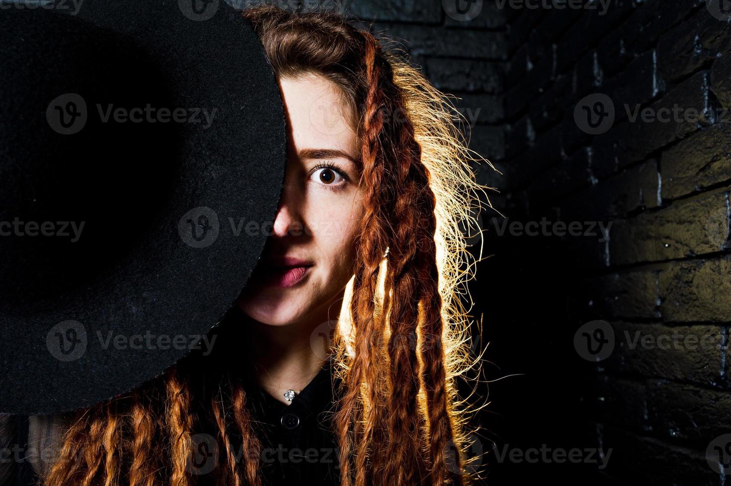 Studio shoot of girl in black with dreads and hat on brick background. photo