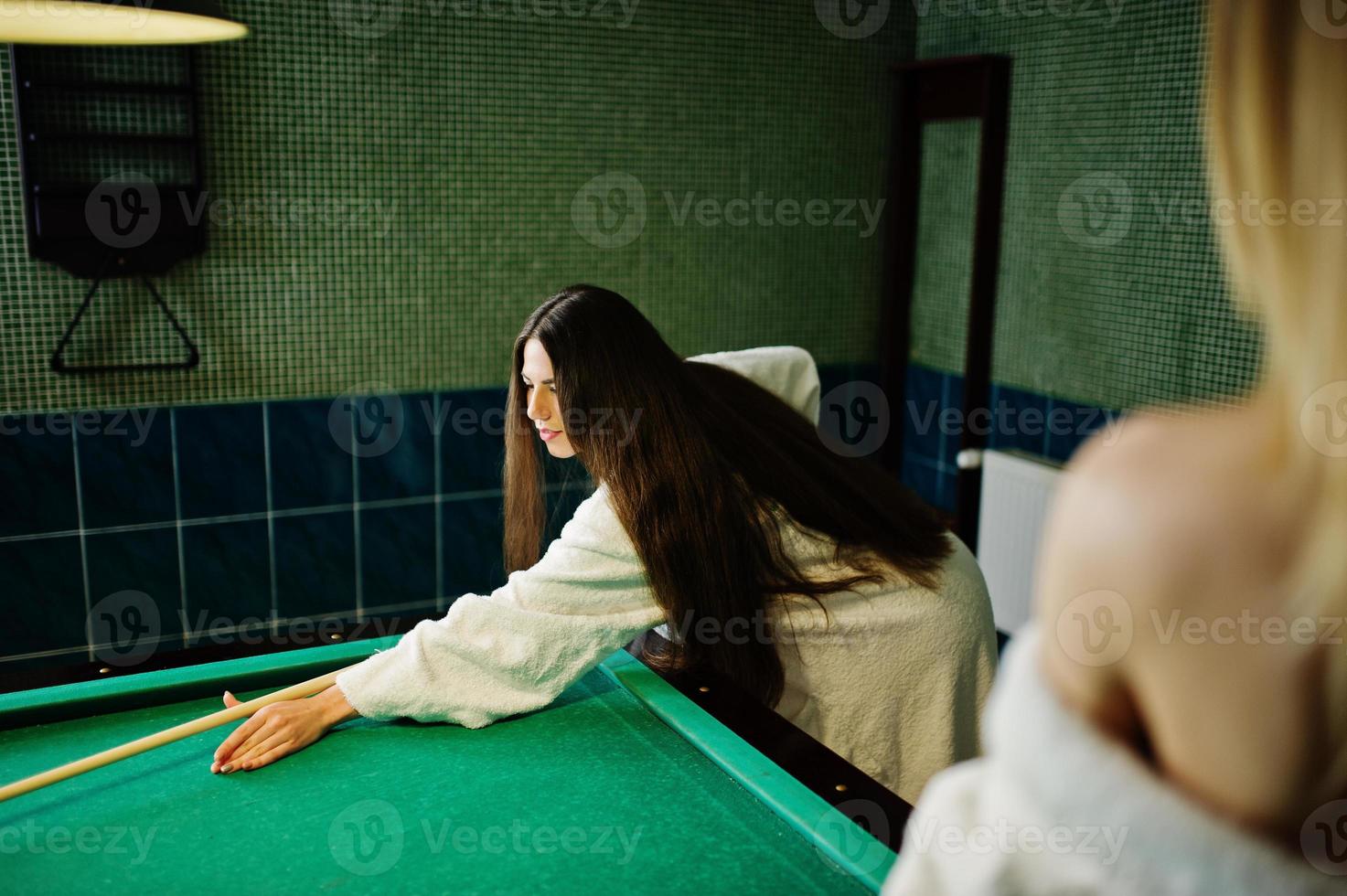 dos chicas sexy en albornoz blanco y traje de baño juegan al billar. foto
