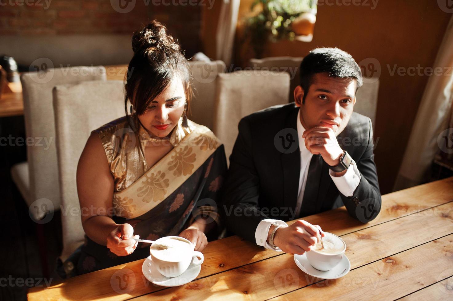 elegante y de moda amigos indios pareja de mujer en sari y hombre en traje sentado en el café y bebiendo capuchino. foto