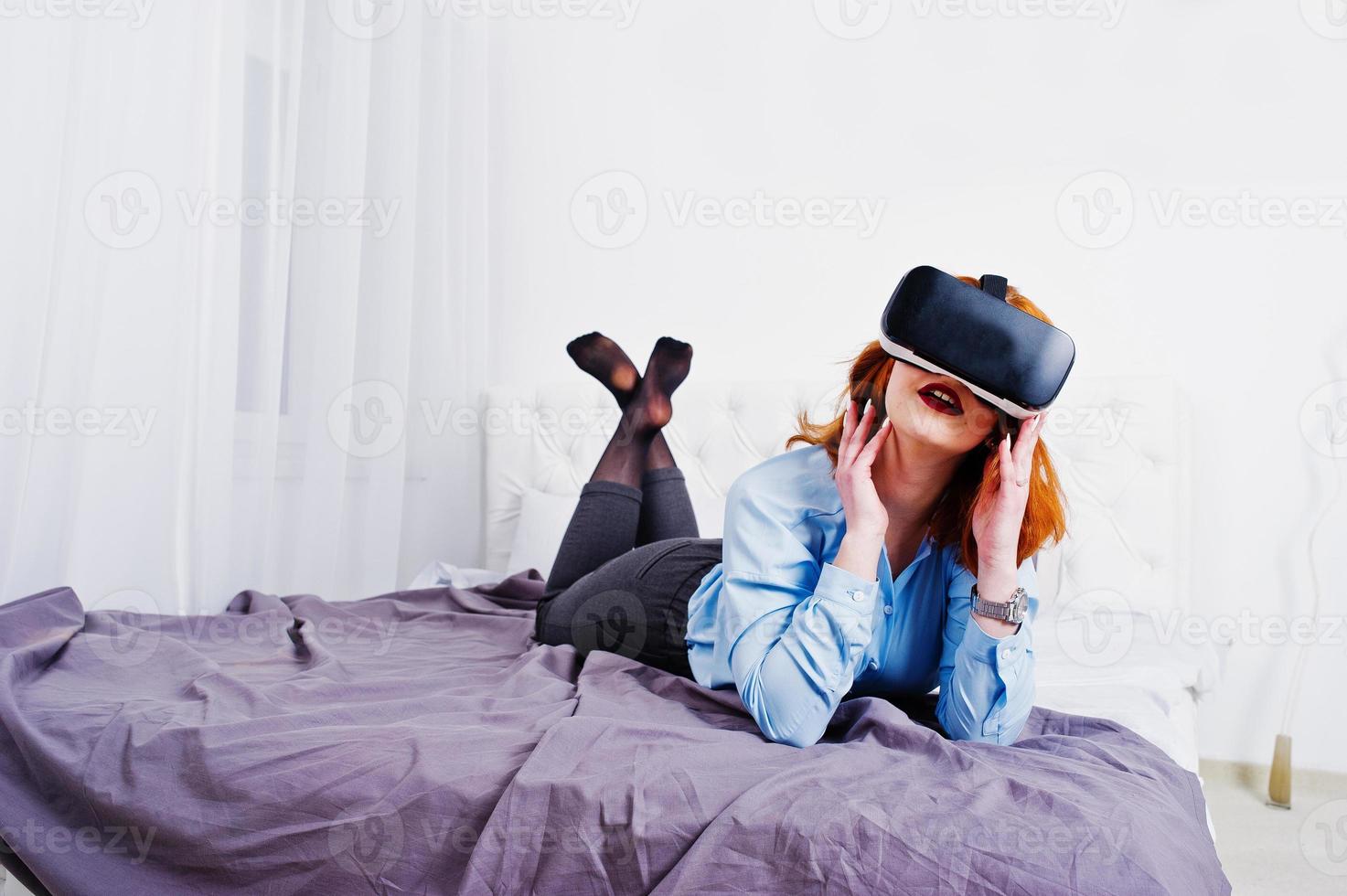 Red haired girl in bed with vr glasses at studio room. photo