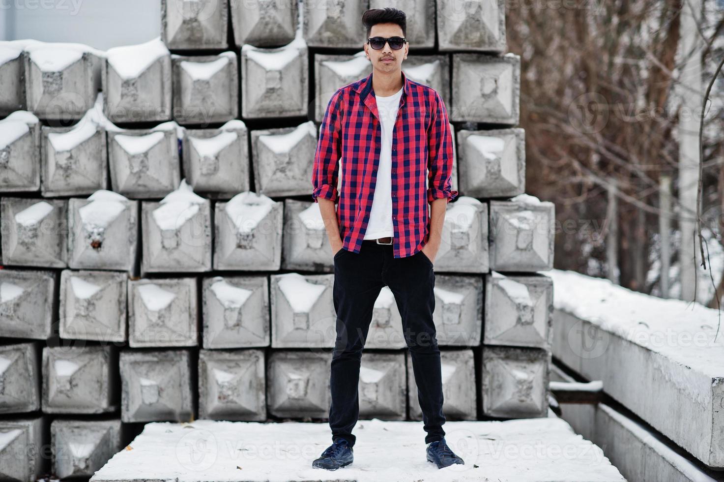 Casual young indian man in checkered shirt and sunglasses posed against stone blocks. photo