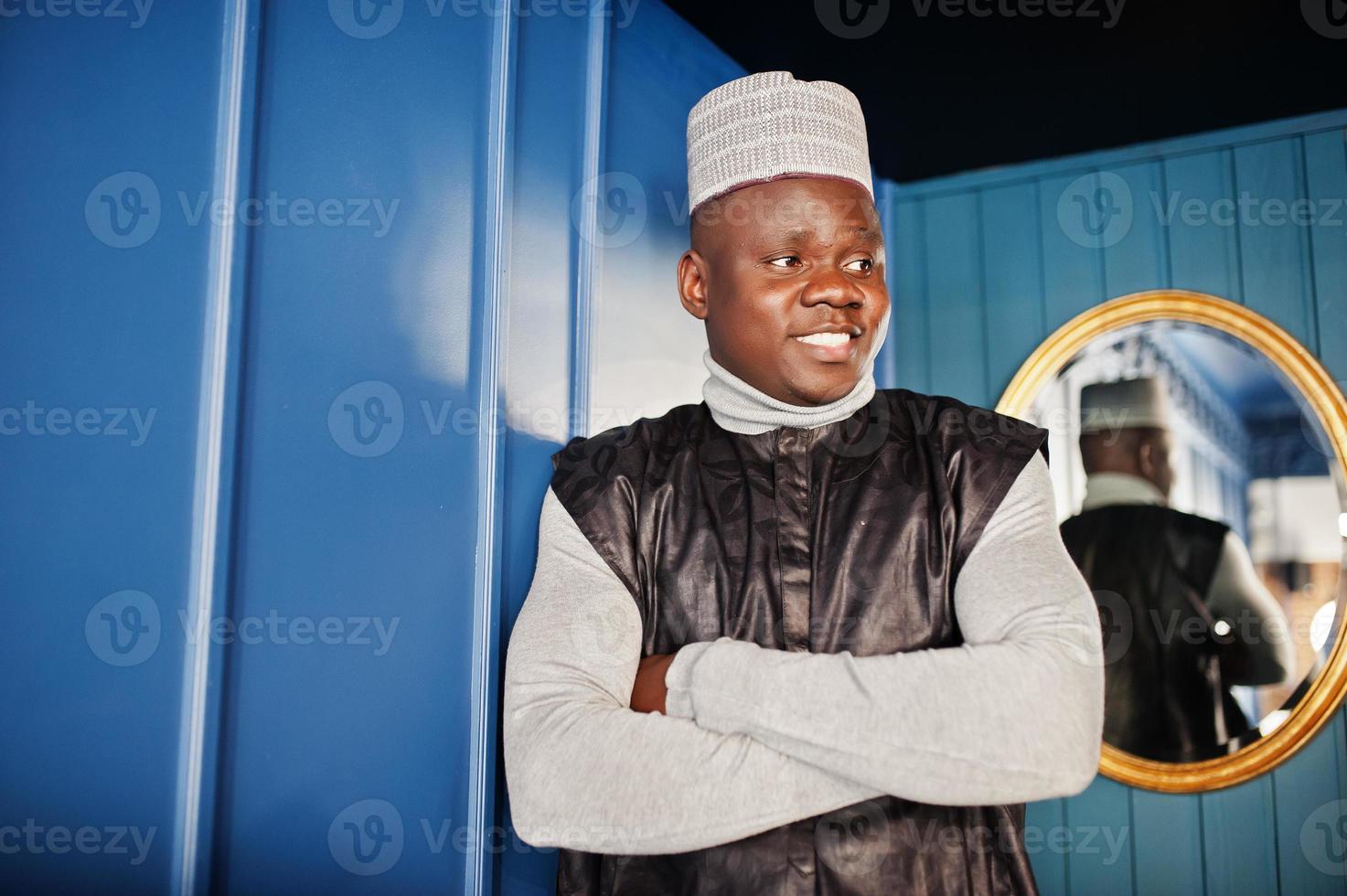 African men in black traditional clothes with cap against mirror on blue wall. photo