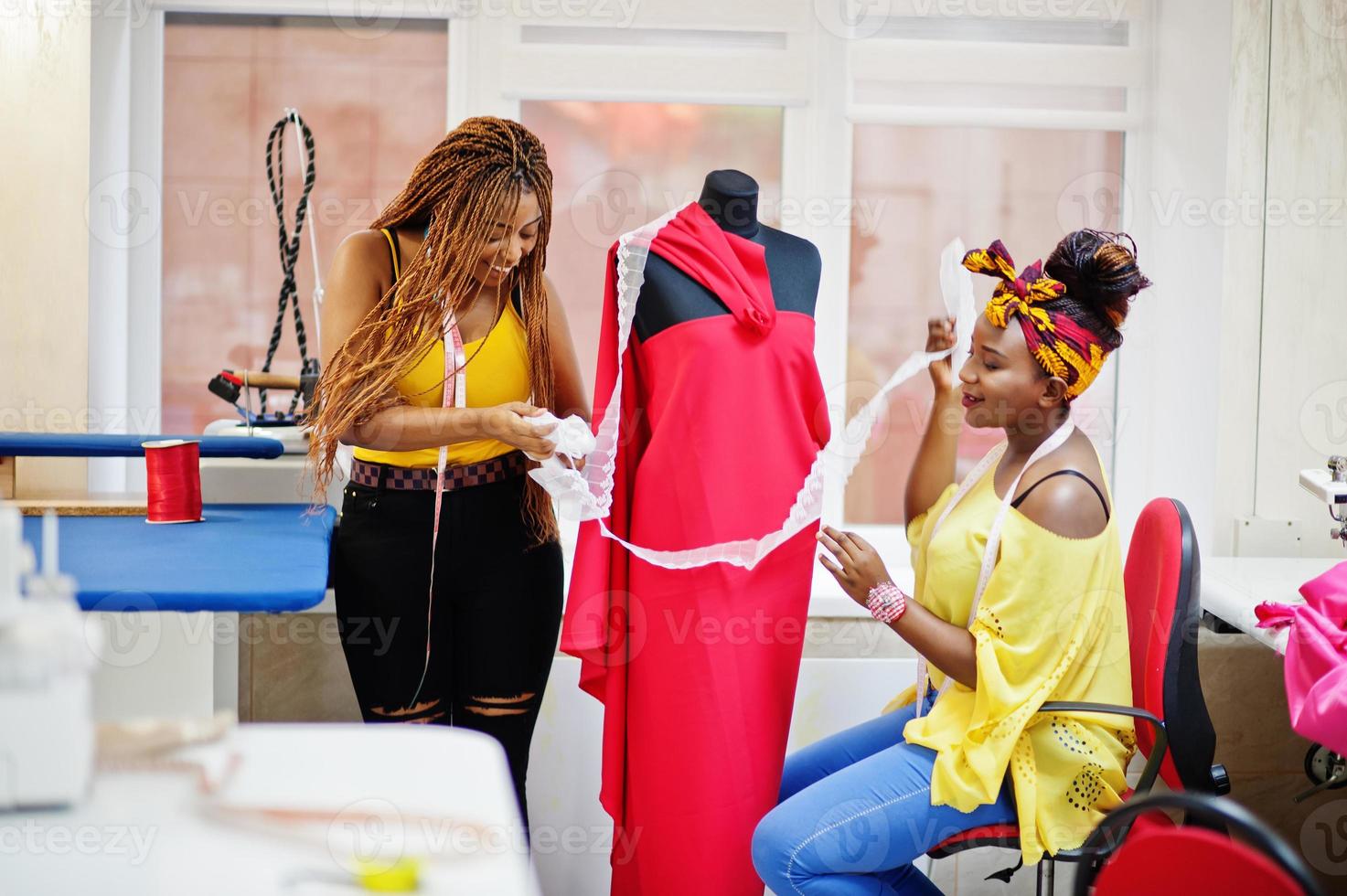 Two african dressmaker woman designed new red dress on mannequin at tailor office. Black seamstress girls. photo