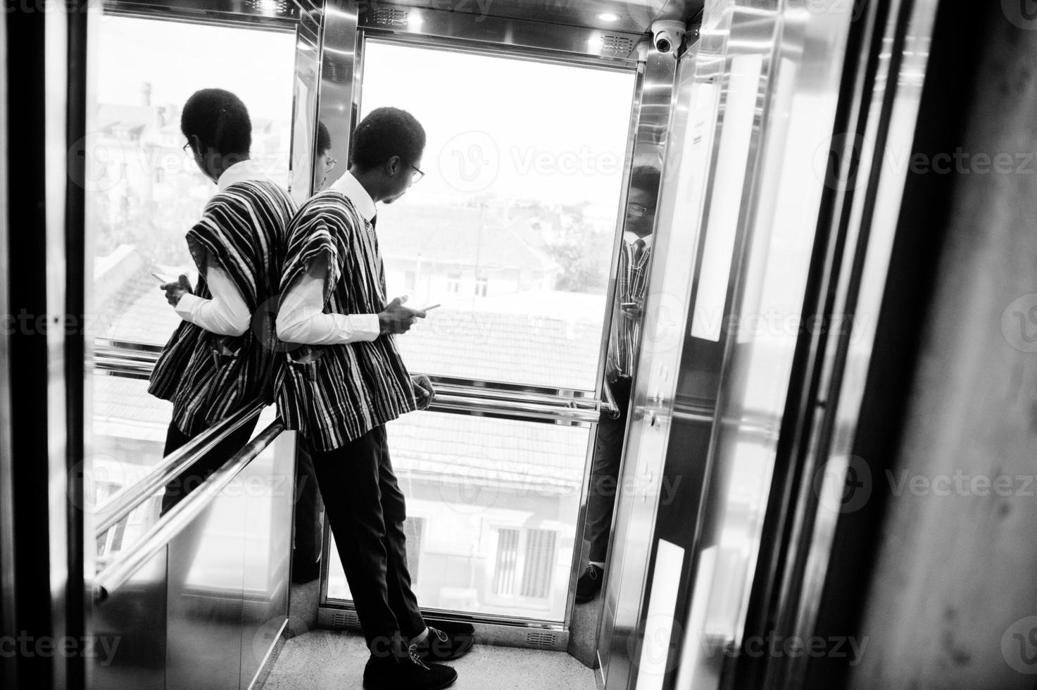 hombre africano con ropa tradicional y gafas con teléfono móvil en elavator o ascensor moderno. foto