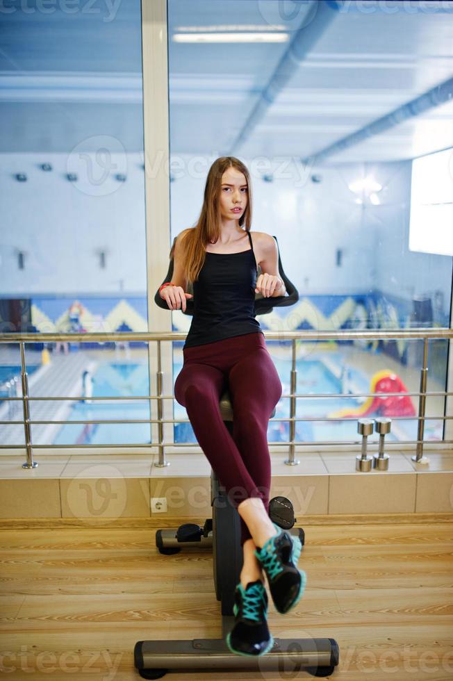 Young sport girl workout in gym. Fitness woman doing exercises on stationary bicycle. photo