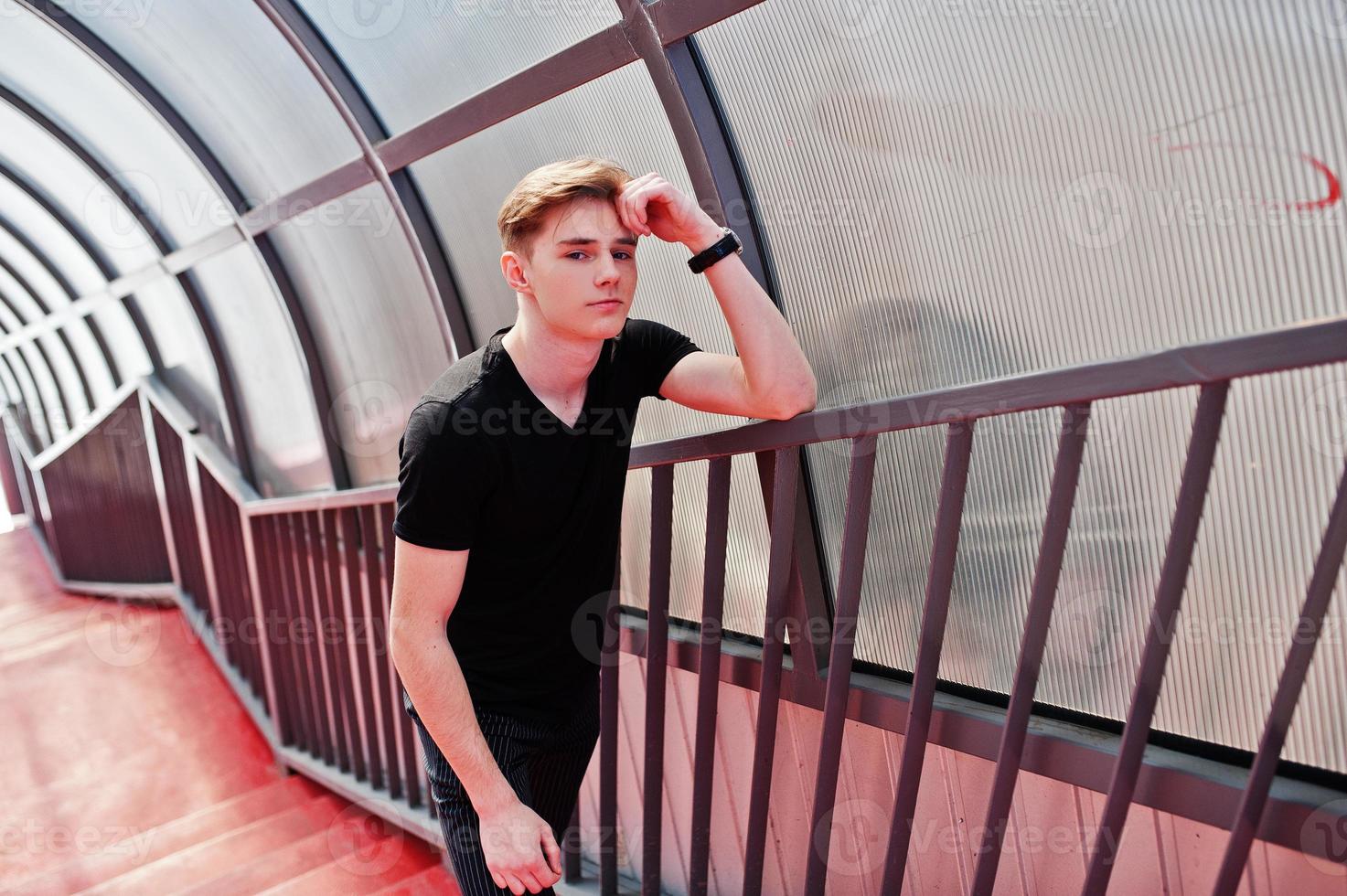 joven macho con estilo en chaqueta negra planteada al aire libre de la calle. increíble modelo de hombre en el tonnel de escaleras rojas. foto