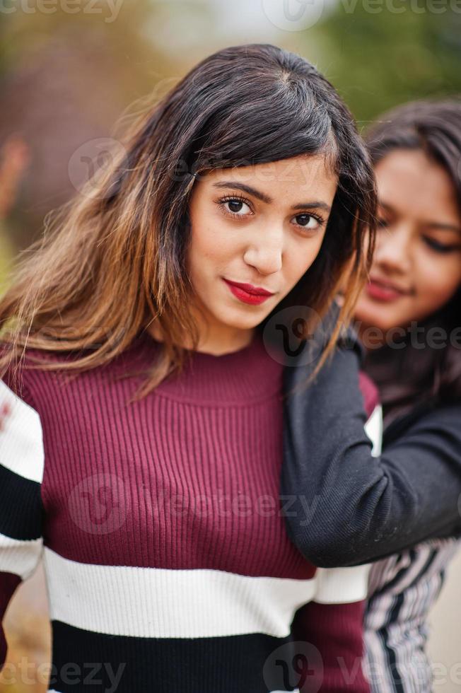 Portrait of two young beautiful indian or south asian teenage girls in dress posed near bushes. photo