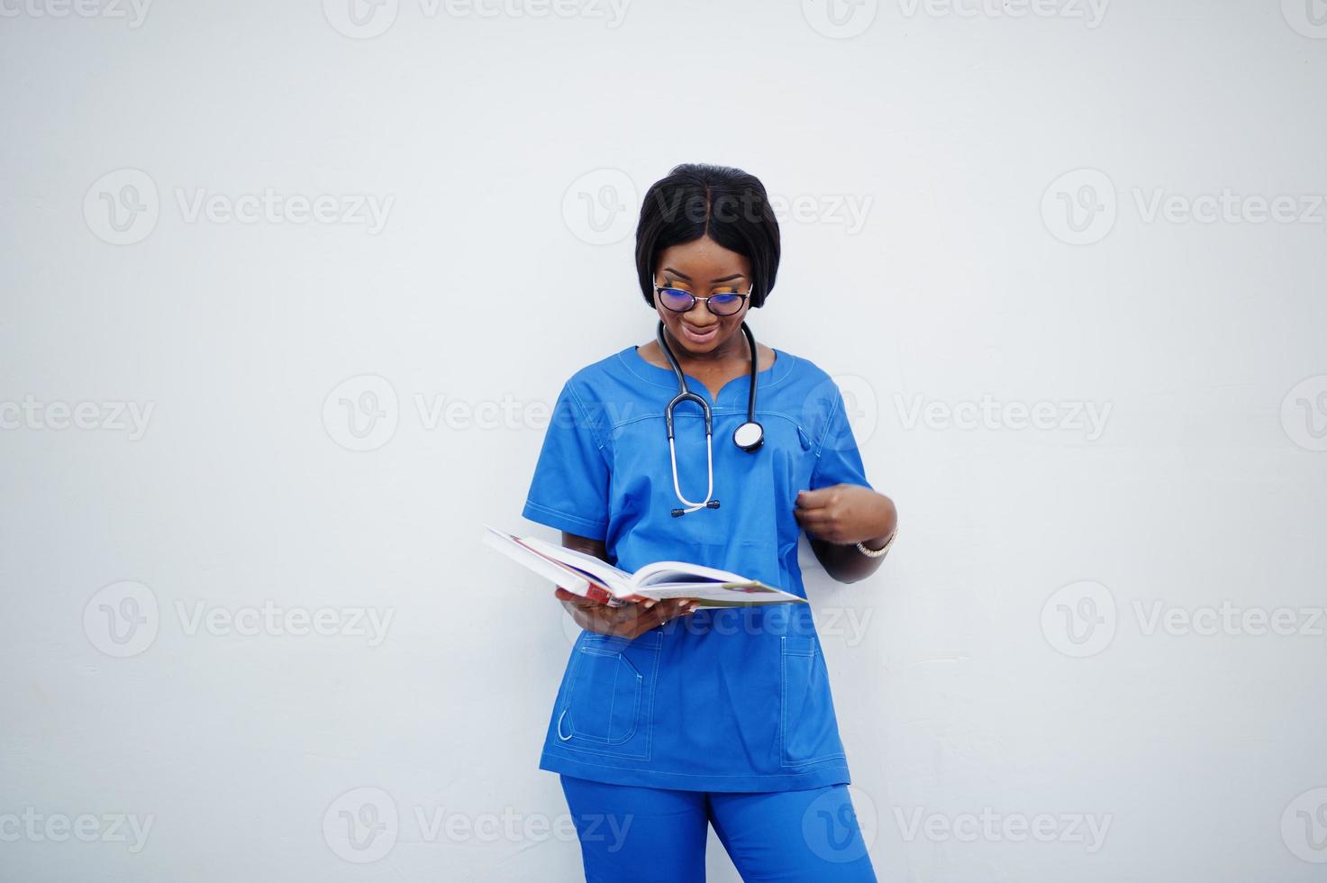 Portrait of happy female african american young doctor pediatrician in blue uniform coat and stethoscope with books at hands isolated on white. photo