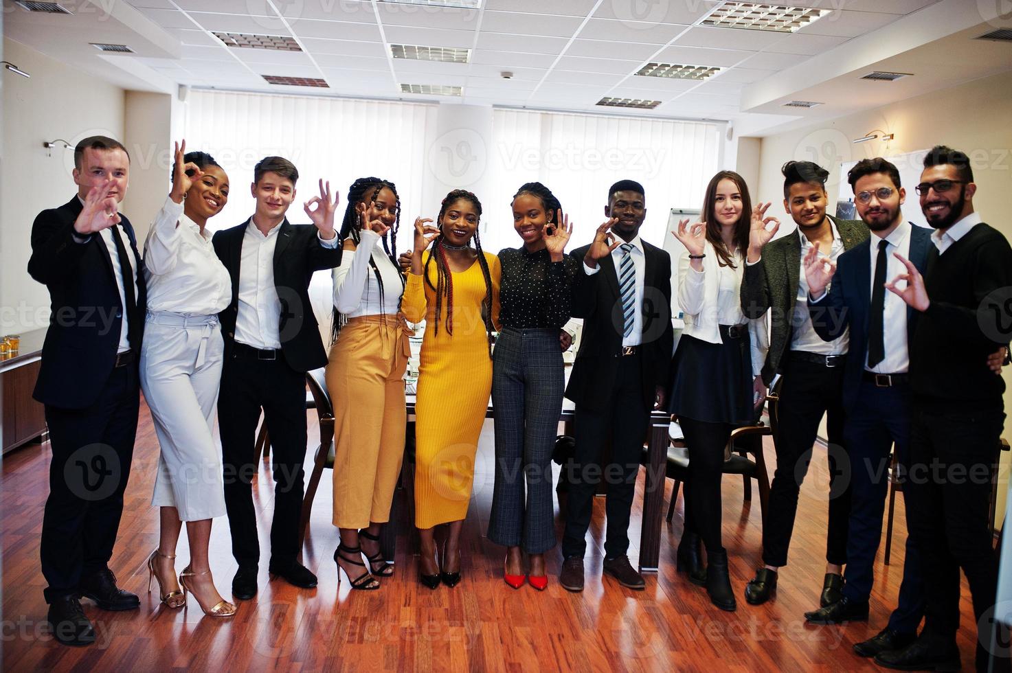 un gran grupo de once empresarios multirraciales parados en la oficina y mostrando juntos el cartel de ok. grupo diverso de empleados en ropa formal. foto