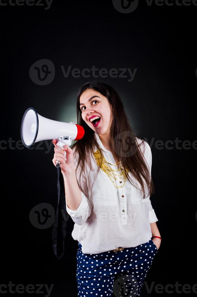 retrato de una mujer joven con pantalones azules y blusa blanca posando con megáfono en el estudio. foto