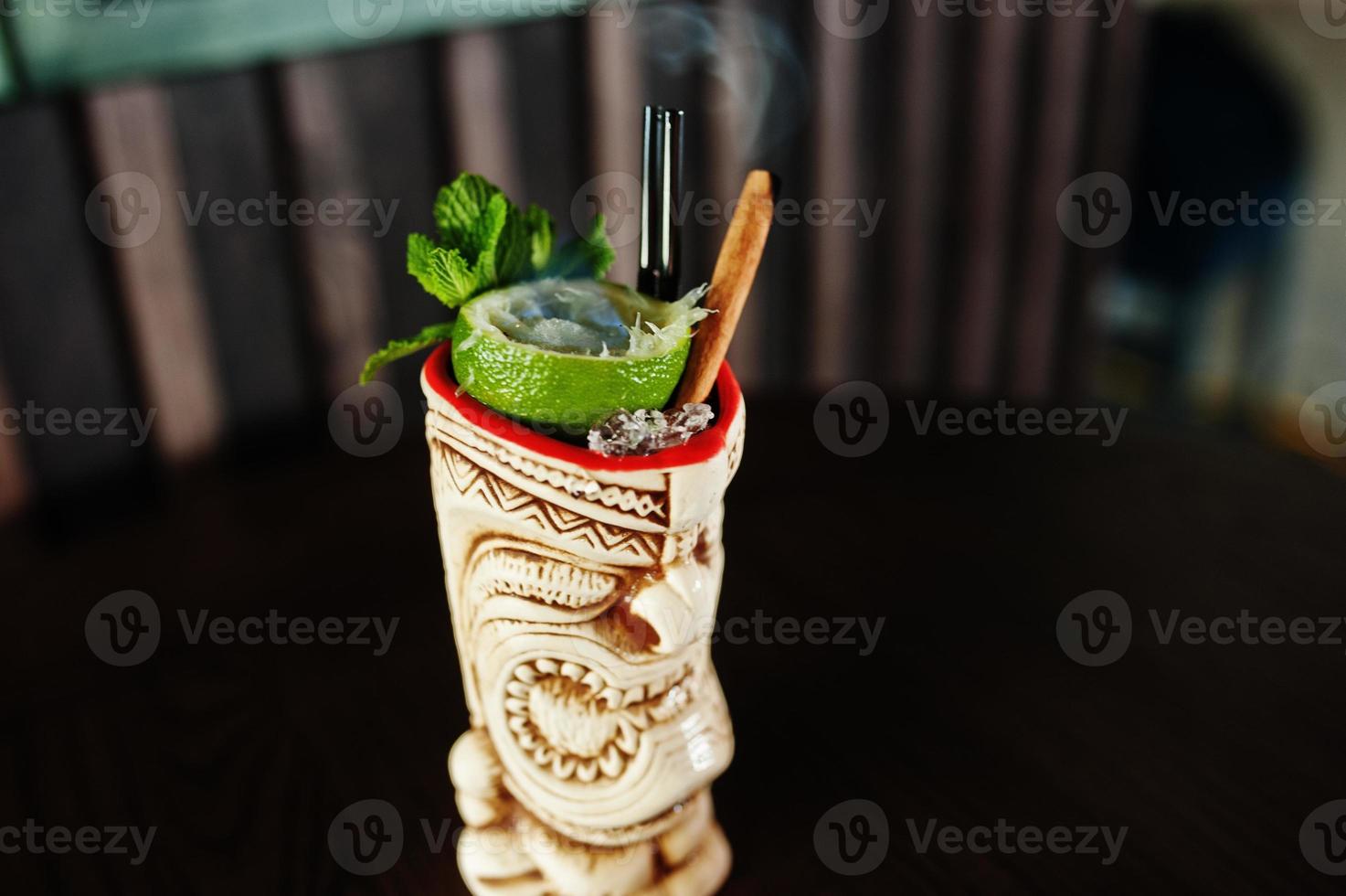 Alcoholic cocktail with mint and lime with fire in originally voodoo earthen glass on bar table. photo