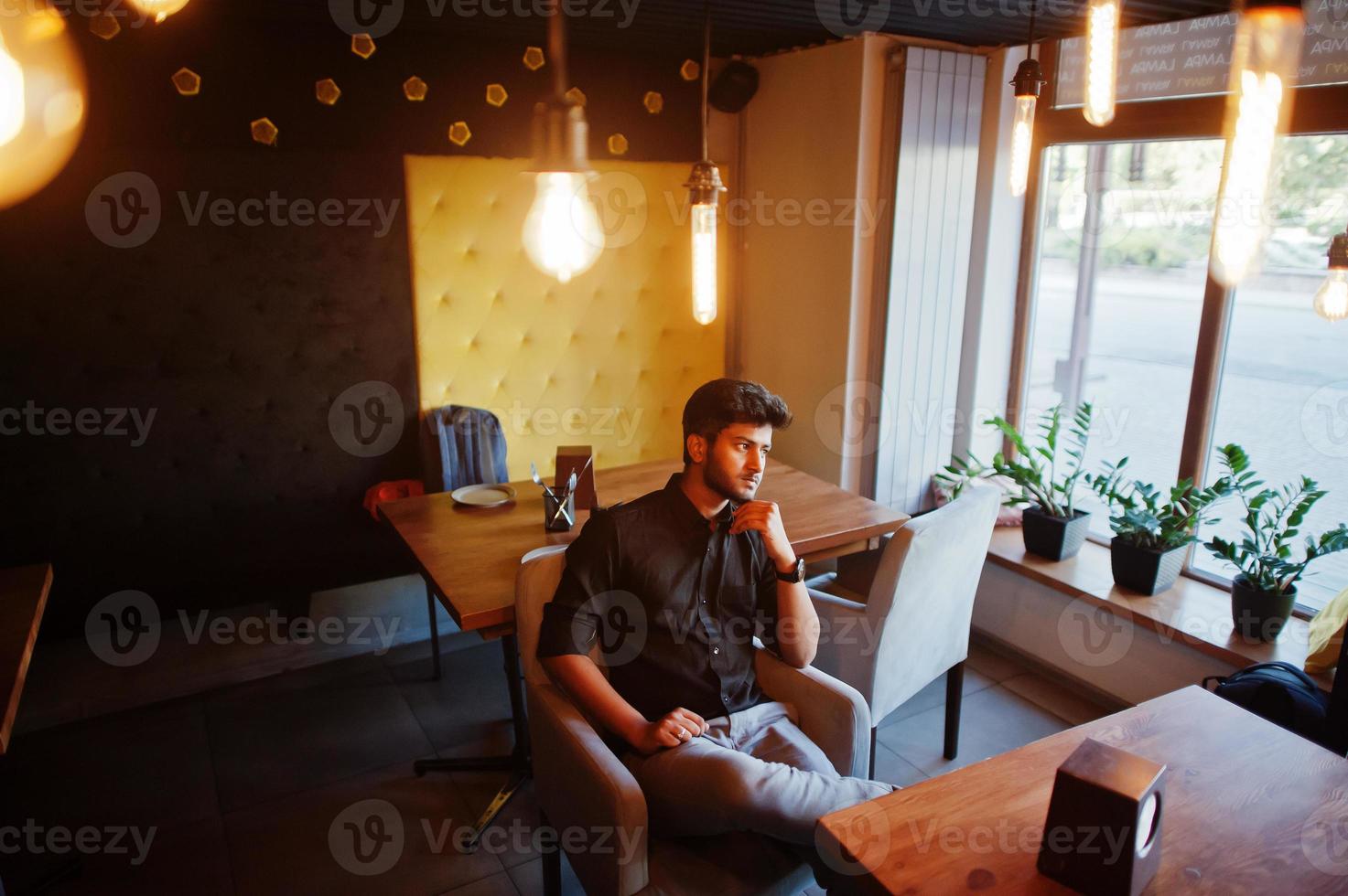 Confident young indian man in black shirt sitting at cafe. photo