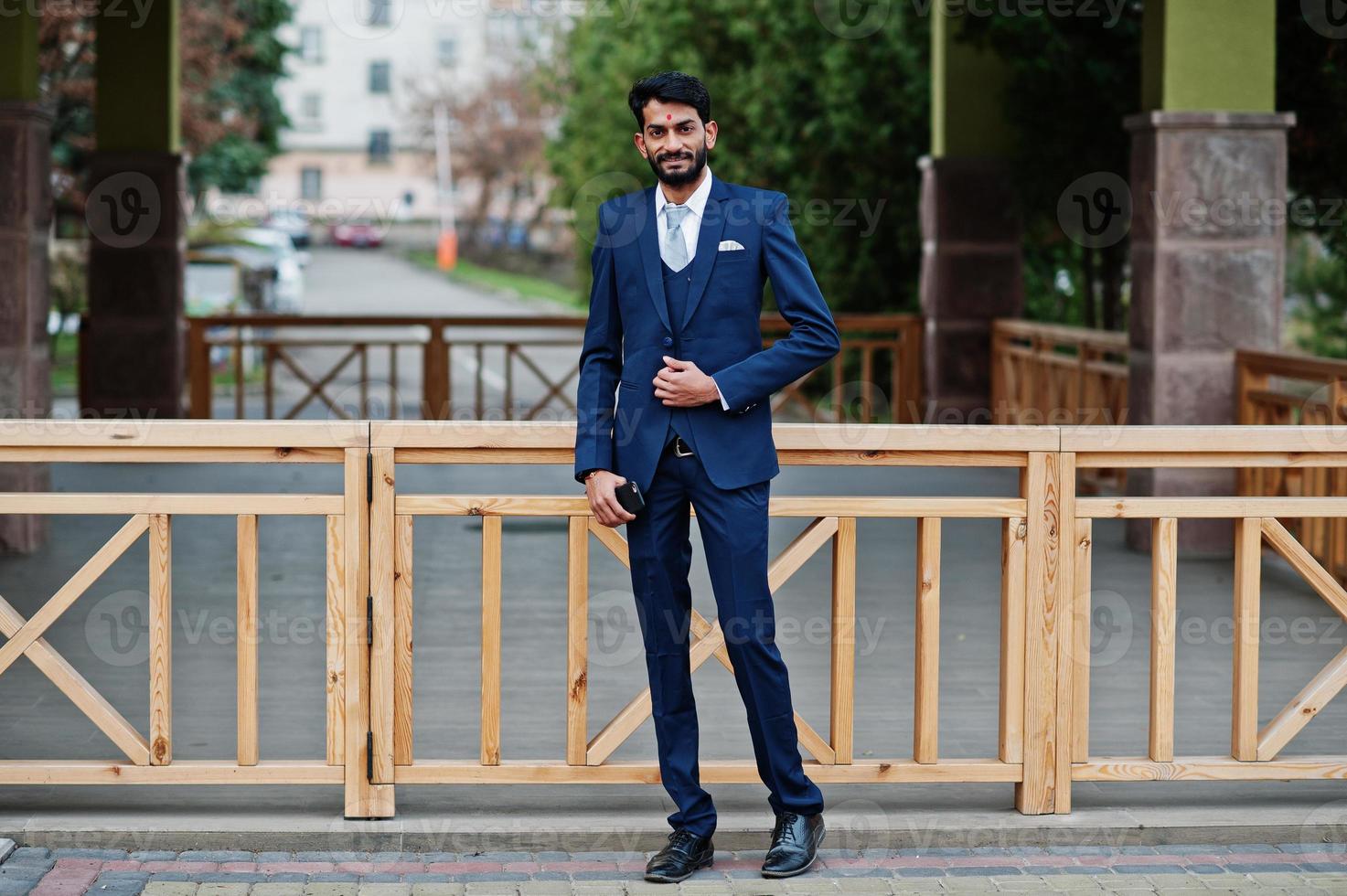 Stylish beard indian man with bindi on forehead, wear on blue suit posed outdoor. photo