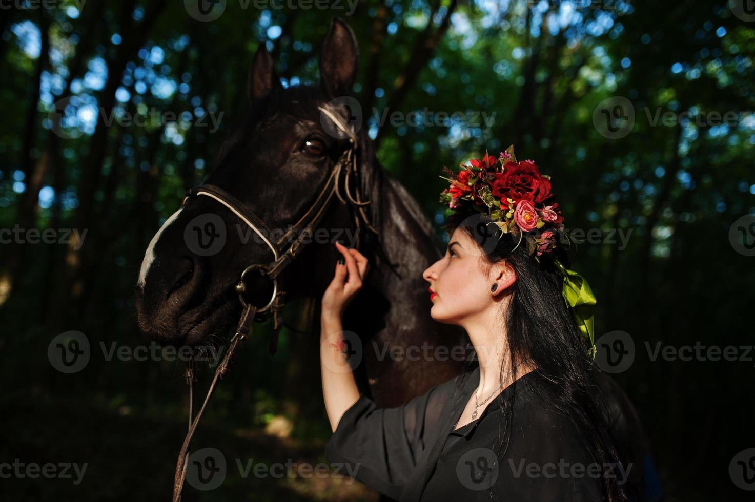 Mystical girl in wreath wear in black with horse in wood. photo