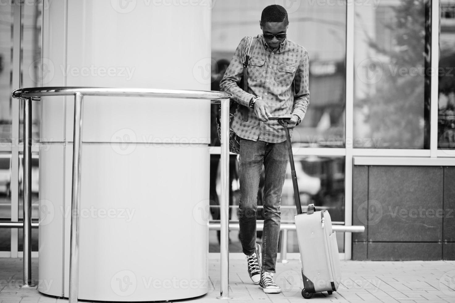 African american man in checkered shirt, with suitcase and backpack. Black man traveler against bus station. photo