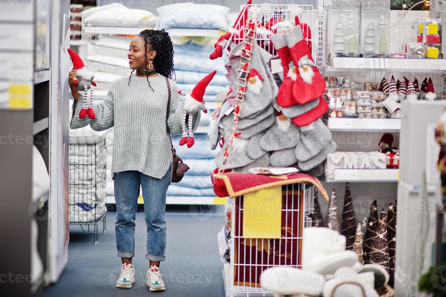 mujer africana eligiendo cosas de año nuevo para su apartamento en una moderna tienda de muebles para el hogar. compras temáticas navideñas. foto