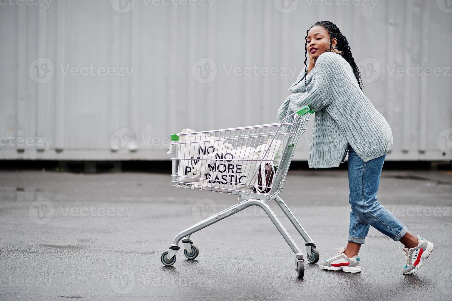 no más plástico. mujer africana con carrito de compras y bolsas ecológicas posadas en el mercado al aire libre. foto