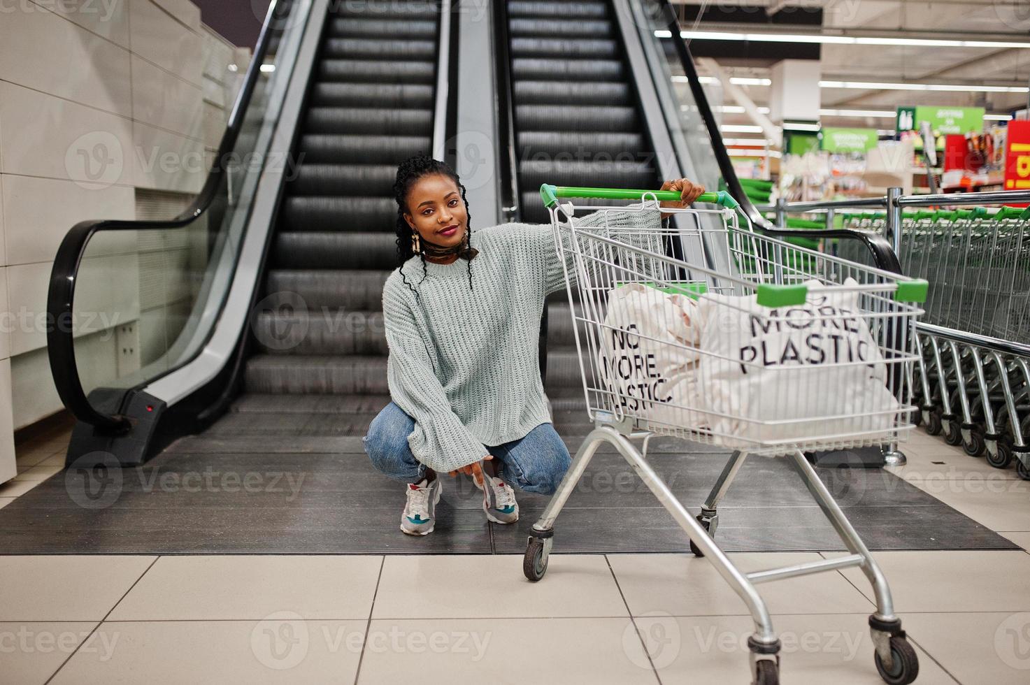 no más plástico. mujer africana con carrito de compras posada en el supermercado contra las escaleras mecánicas. foto