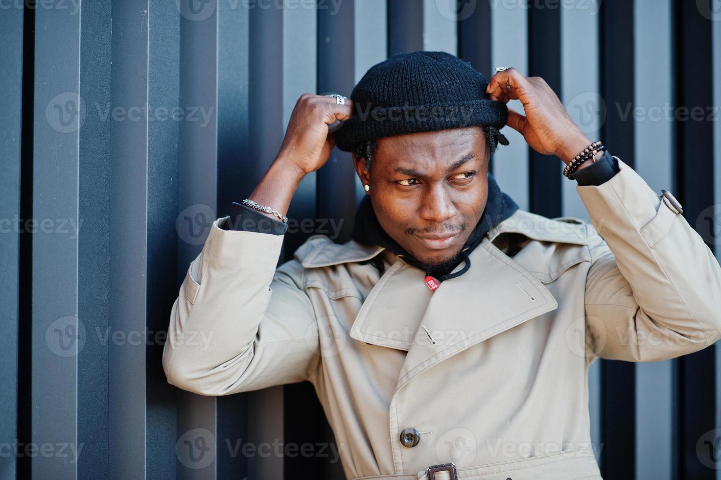 Handsome african american man posing outside in black hat and beige coat. photo