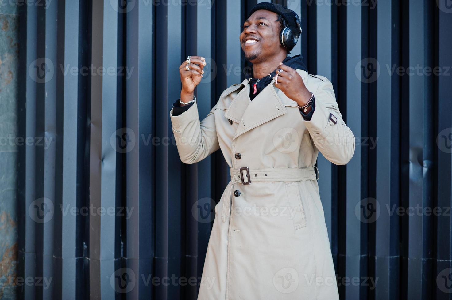 African american man with headphones, wear on hat and coat listening music on steel background. photo