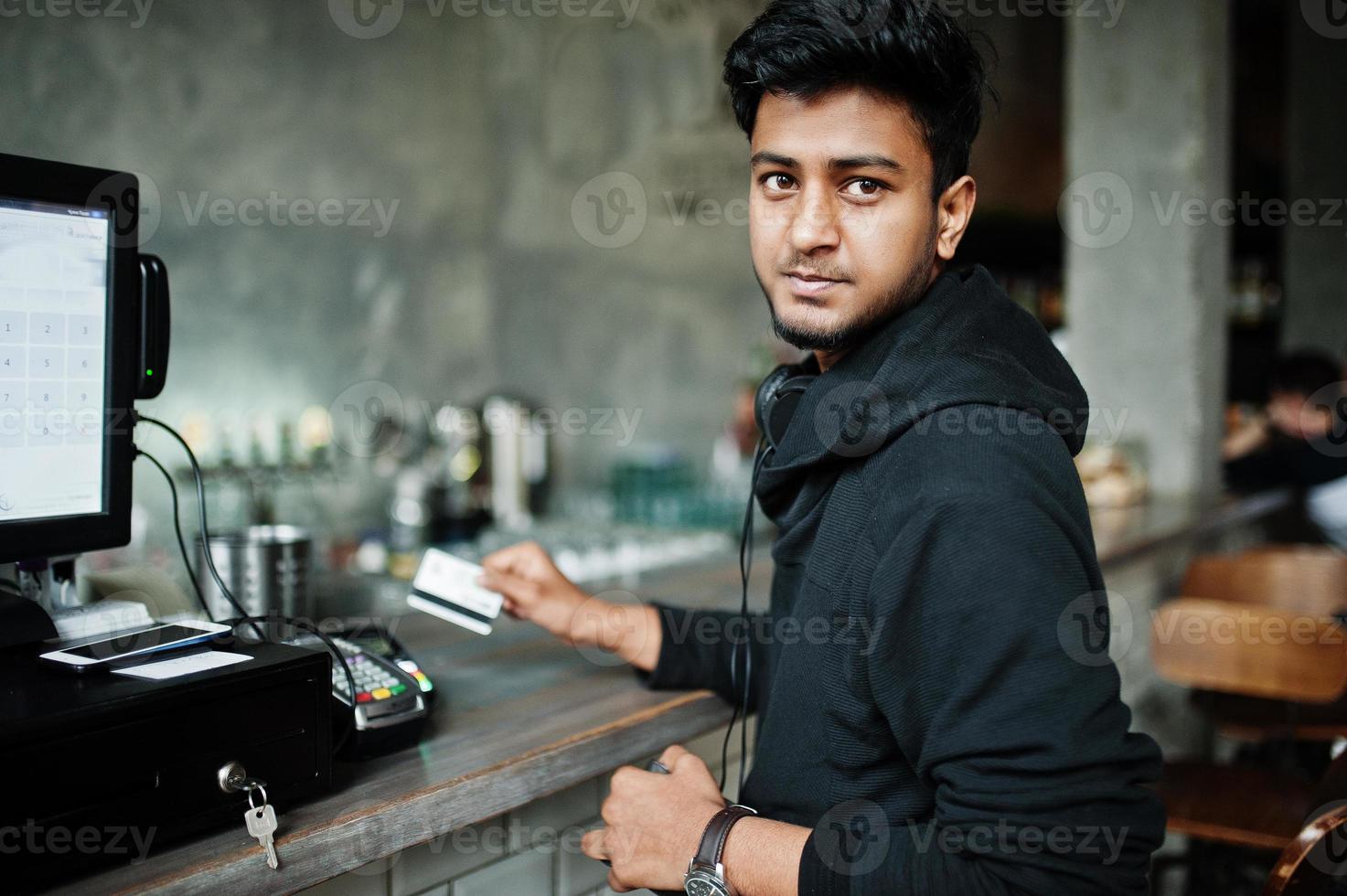 Casual and stylish young asian man with earphones at cafe on bar paying by credit card on pos terminal. photo