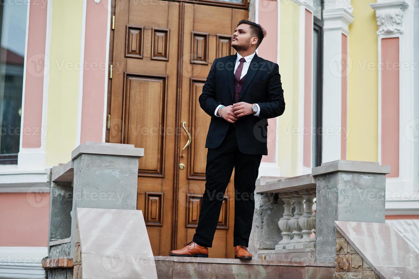 Stylish indian businessman in formal wear standing against door in business center. photo